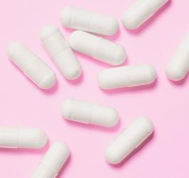 Białe kapsułki na różowym tle.
