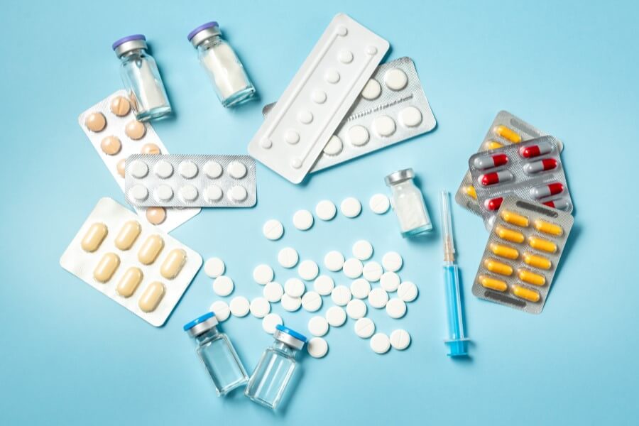 Tabletki, kapsułki, fiolki i strzykawki na błękitnym tle.