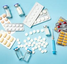 Tabletki, kapsułki, fiolki i strzykawki na błękitnym tle.