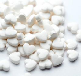Białe tabletki w kształcie serca rozsypane na jasnym tle.