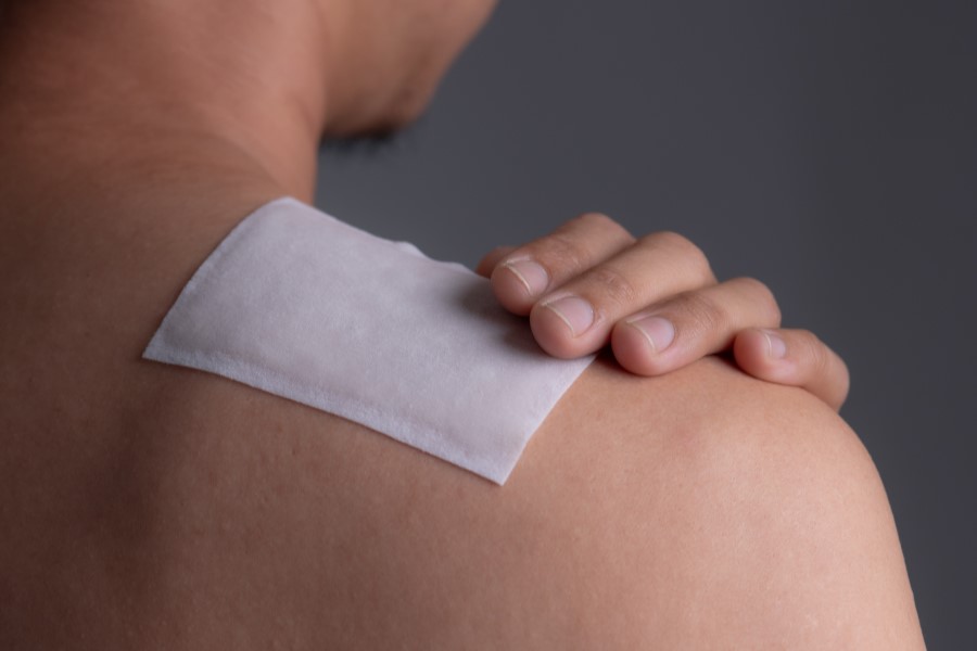Mężczyzna nakleja na bark plaster przeciwbólowy.