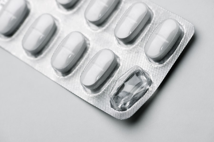 Blister z białymi tabletkami na szarym tle.