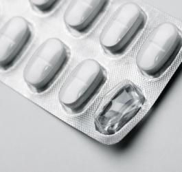 Blister z białymi tabletkami na szarym tle.