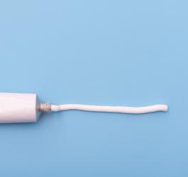 Maść lecznicza wyciśnięta z białej tubki, tworząca linię na niebieskim tle.