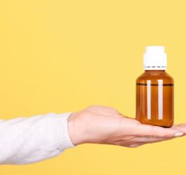 Kobieta trzyma na dłoni butelkę z brązowego szkła z biała nakrętką.