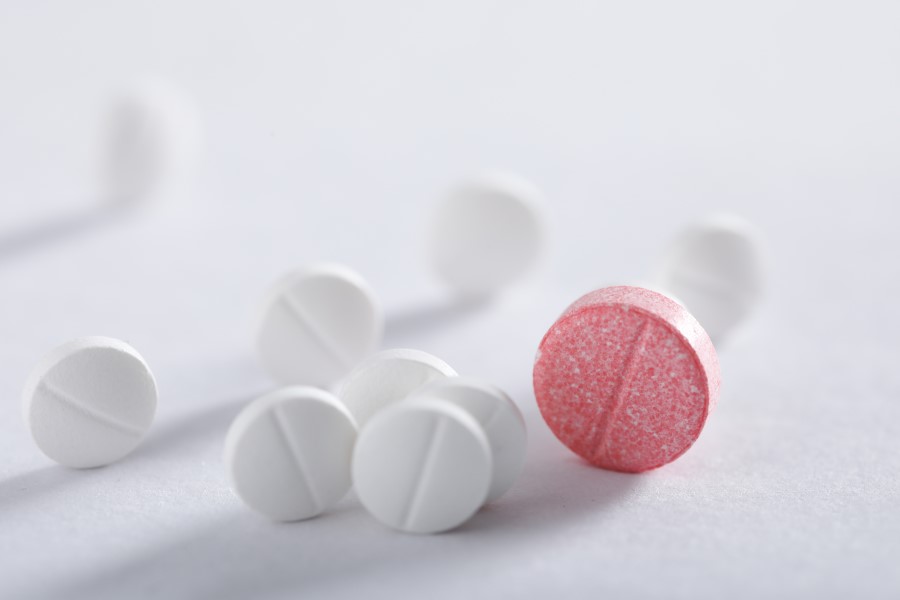 Białe tabletki z podziałką, wśród nich duża, czerwona tabletka z podziałką.