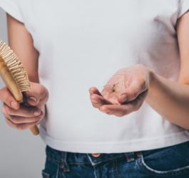 Kobieta wyciąga ze szczotki kępki włosów, które świadczą o nadmiernym wypadaniu włosów.