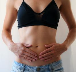 Kobieta trzyma się dłońmi za brzuch, dokuczają jej wzdęcia.