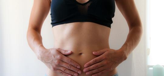 Kobieta trzyma się dłońmi za brzuch, dokuczają jej wzdęcia.