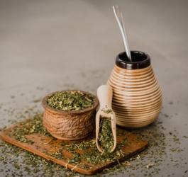 Susz yerba mate na drewnianej desce oraz matero z bombillą i gotowym naparem z yerby.