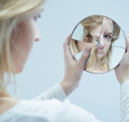 Kobieta spogląda w rozbite lusterko.