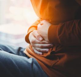 Kobieta siedzi na parapecie okiennym i trzyma się za brzuch, choruje na zapalenie jelita grubego.