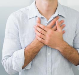Mężczyzna w białej koszuli, jego dłonie są skrzyżowane na klatce piersiowej, w okolicy serca.
