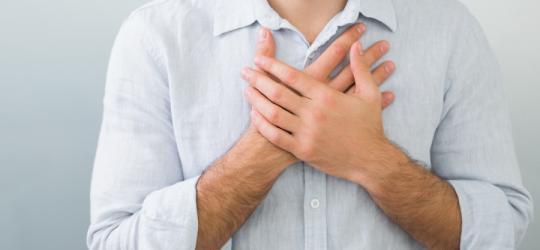 Mężczyzna w białej koszuli, jego dłonie są skrzyżowane na klatce piersiowej, w okolicy serca.