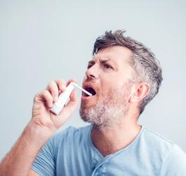 Mężczyzna aplikuje do gardła lek w sprayu, aby zmniejszyć objawy zapalenia migdałków.