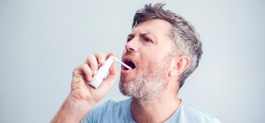Mężczyzna aplikuje do gardła lek w sprayu, aby zmniejszyć objawy zapalenia migdałków.