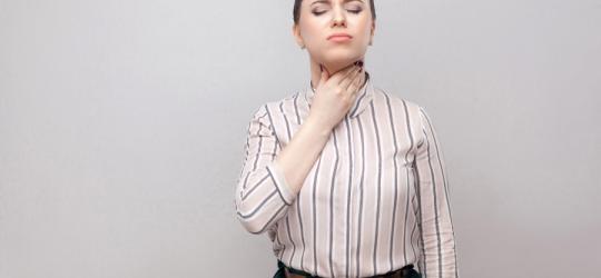 Kobieta trzyma się za bolące gardło, ma zapalenie tchawicy.