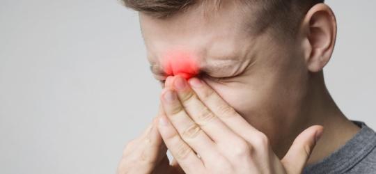 Mężczyzna trzyma się za okolicę nosa. Odczuwa ból, gdyż cierpi na zapalenie zatok przynosowych.