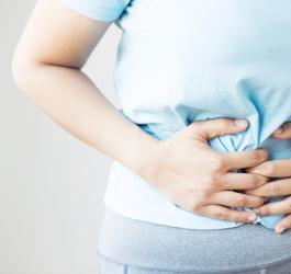 Kobieta trzyma się za bolący brzuch, cierpi na zapalenie błony śluzowej żołądka.