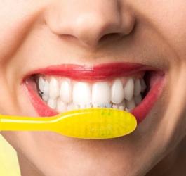 Kobieta szczotkuje zęby żółtą szczoteczką.