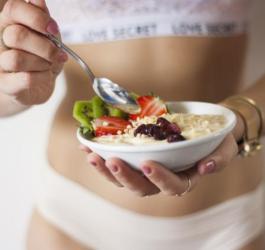 Kobieta trzyma w ręce miseczkę owsianki udekorowaną bakaliami i świeżymi owocami.