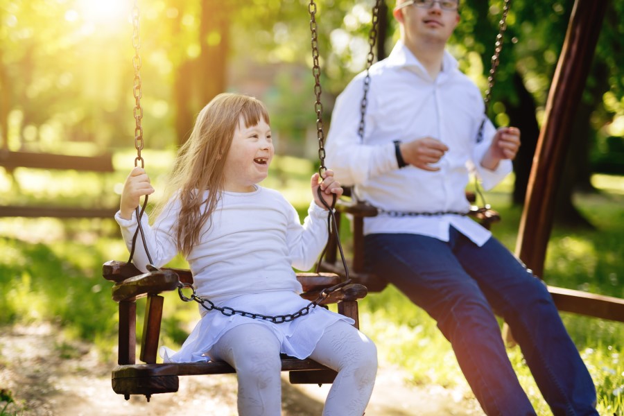 Dziewczyna i mężczyzna z zespołem Downa, bawią się razem na huśtawkach.