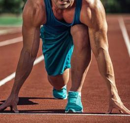 Wysportowany mężczyzna w pozycji startowej na bieżni, jest gotowy do biegu.