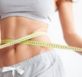 Kobieta mierzy swoją talię przy pomocy metra krawieckiego.