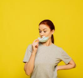 Żółte tło. Kobieta ściąga z twarzy maseczkę jednorazową.