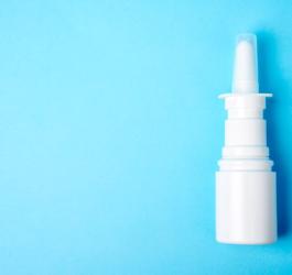 Biała butelka aerozolu do nosa na błękitnym tle.