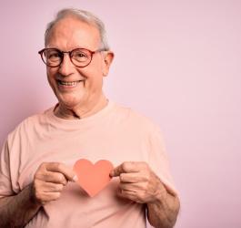 Starszy mężczyzna trzyma na wysokości klatki piersiowej wycięte z papieru serce.